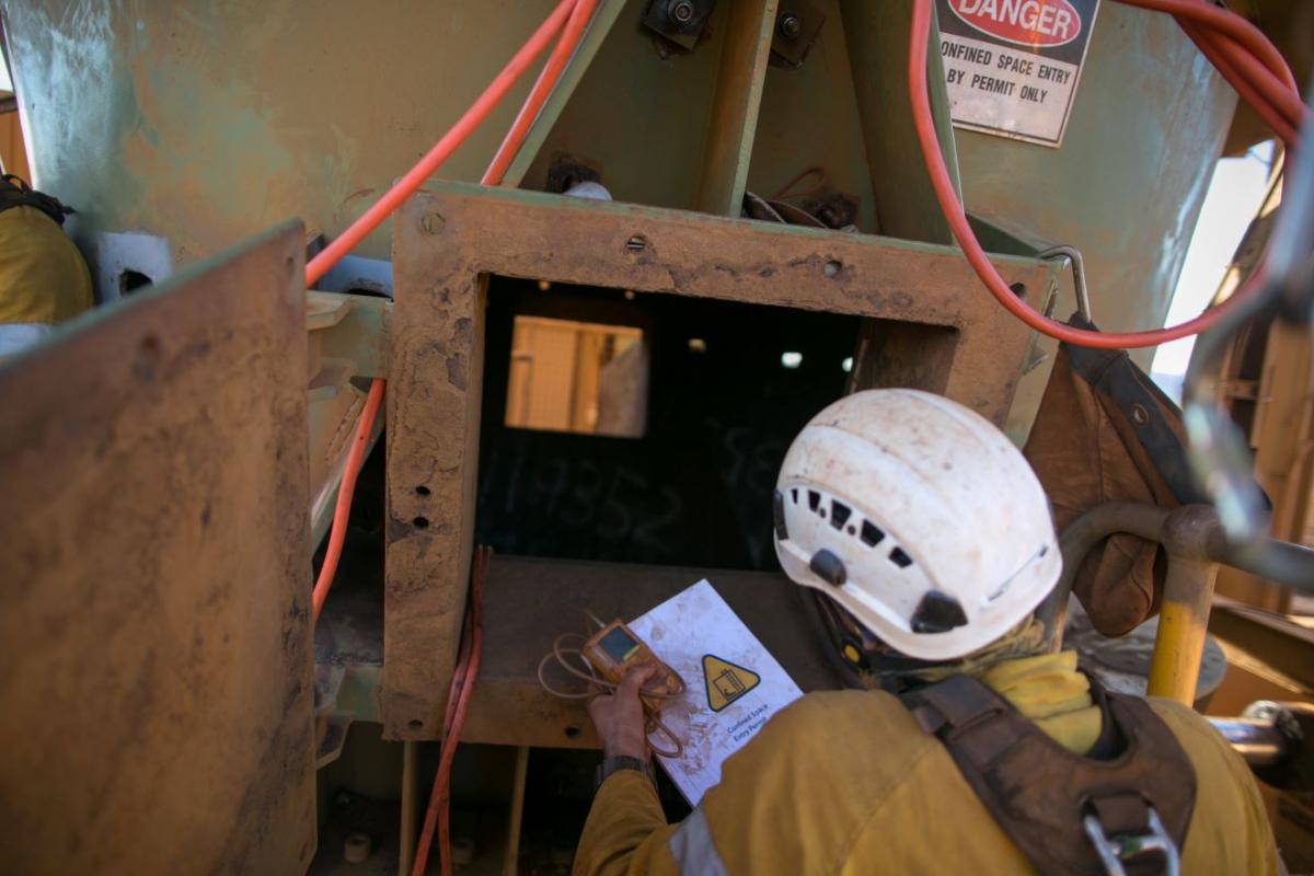 lavoratore di spalle con caschetto davanti a spazio confinato in mano ha una checklist 
